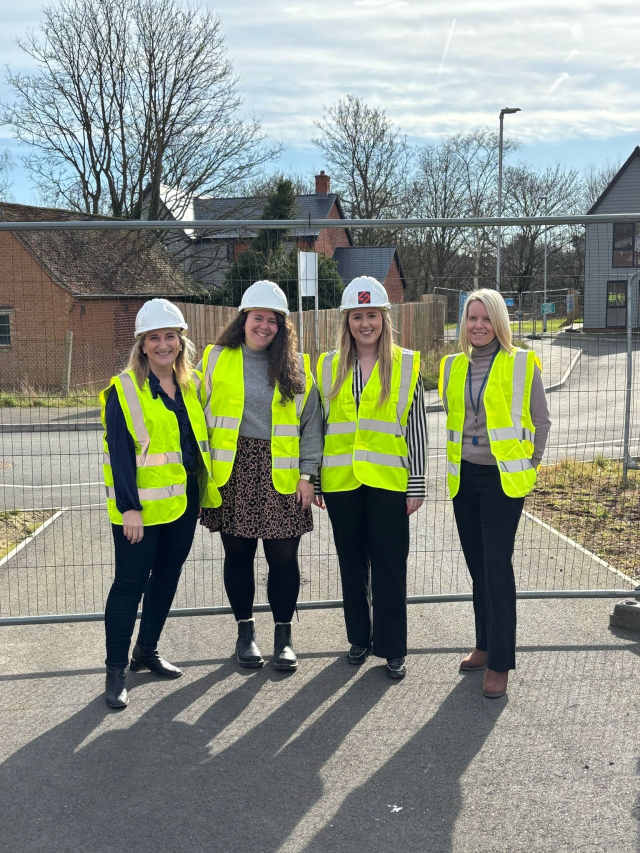 Four professionals wearing high-visibility vests and hard hats standing in front of a construction site fence, representing town planning consultants at work.